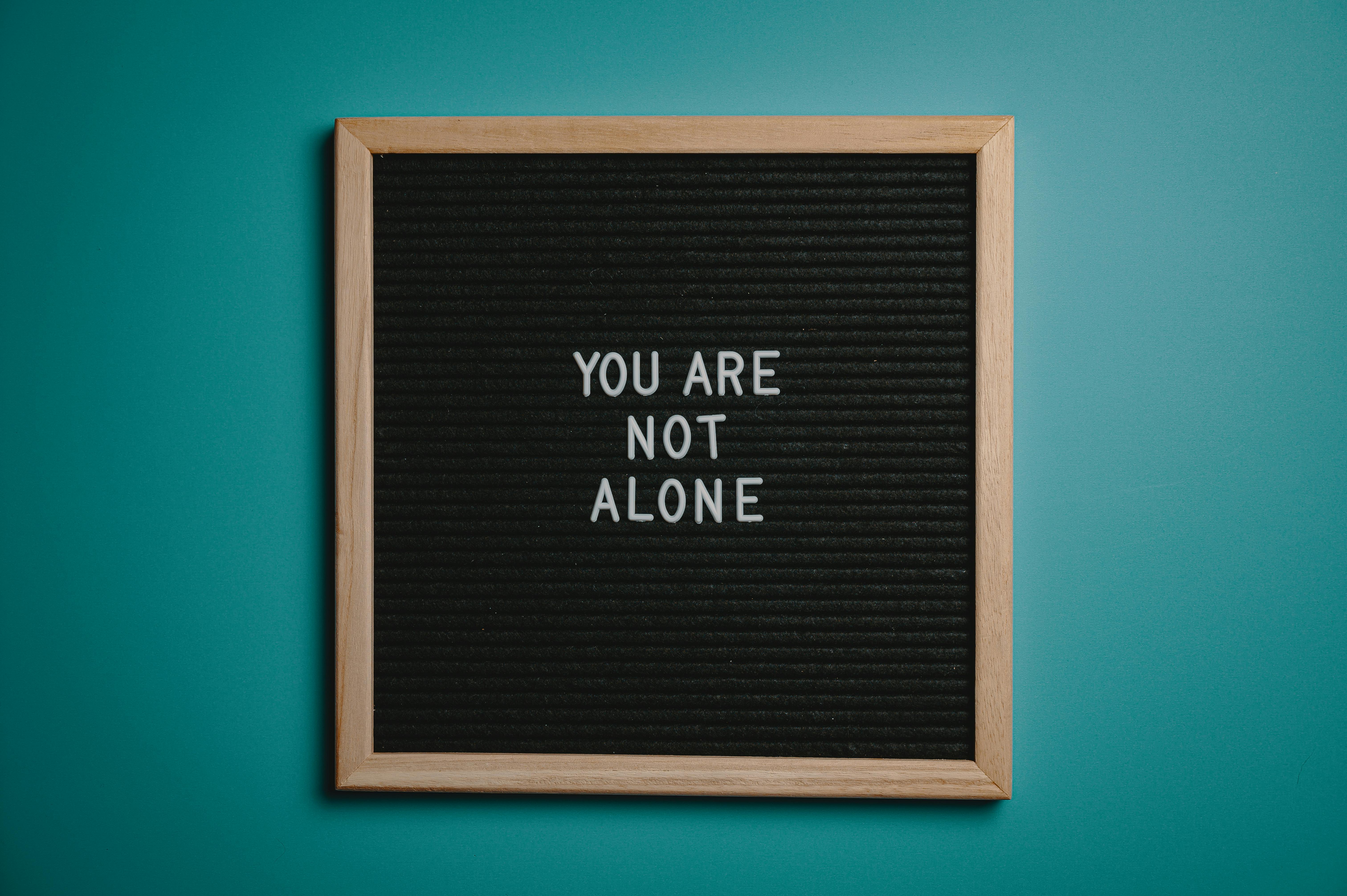 Black letter board with white letters saying you are not alone. wooden frame. blue teal background.