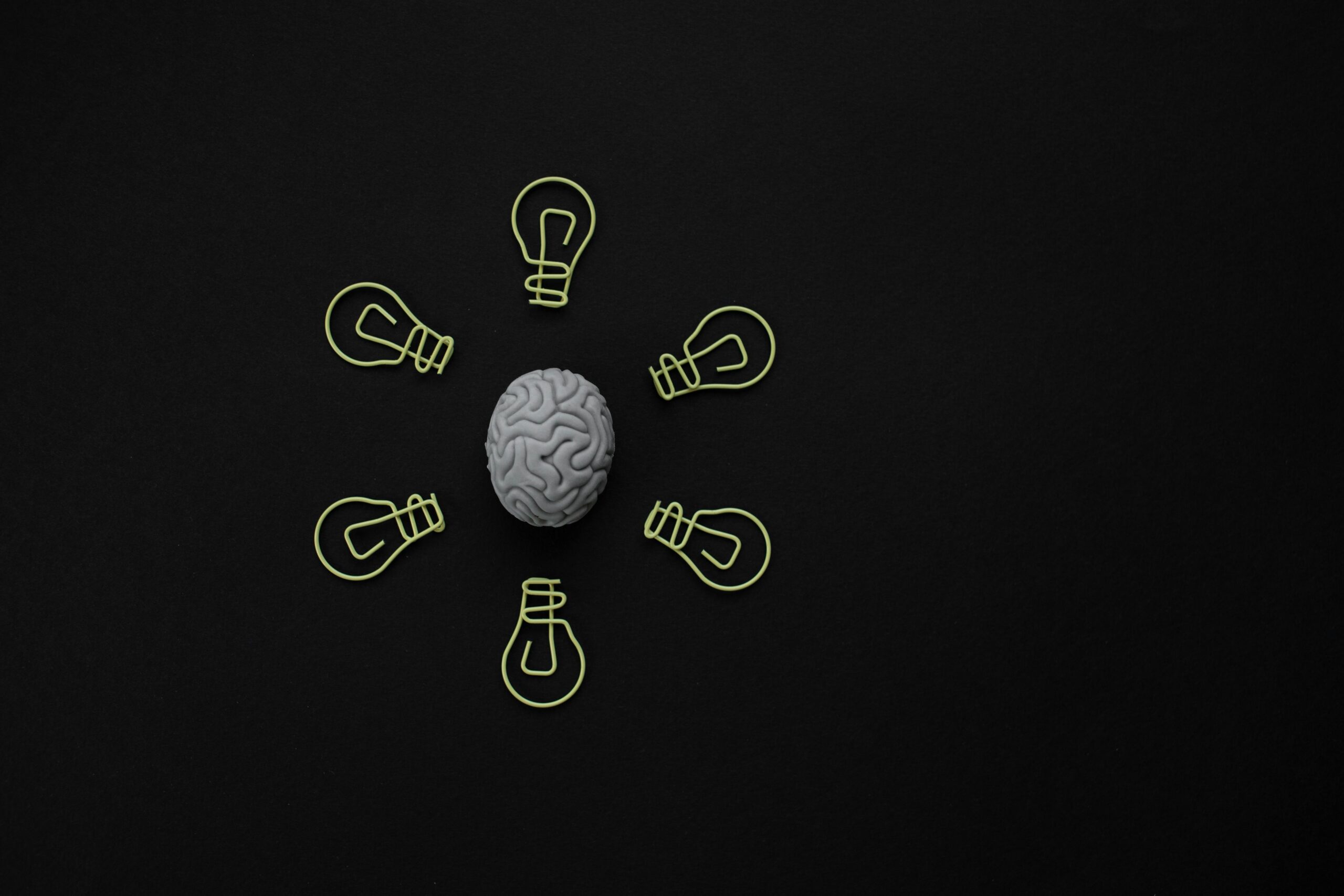 black background with a grey brain in the center with sketched yellow lightbulbs, 6 of them, around the brain