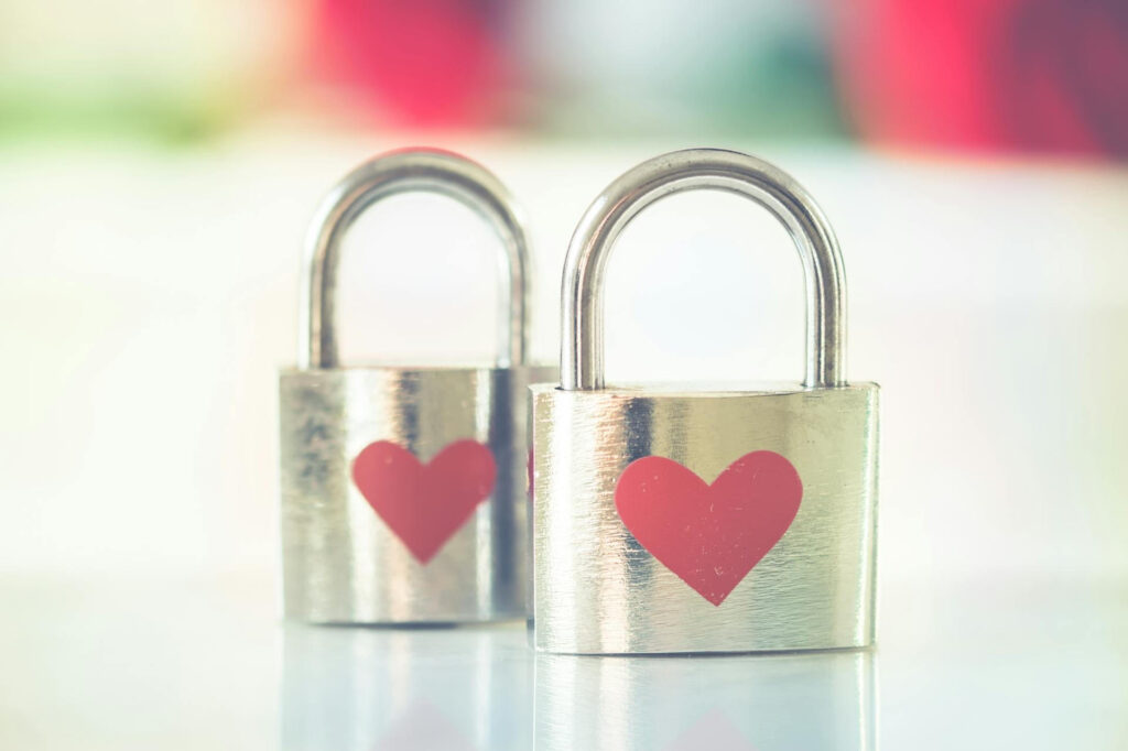 A faded photos of two silver locks with red hearts on them against a blurred multi colored background